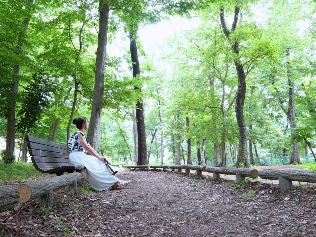 女性が森の中のベンチに座り、遠くを見ている写真
