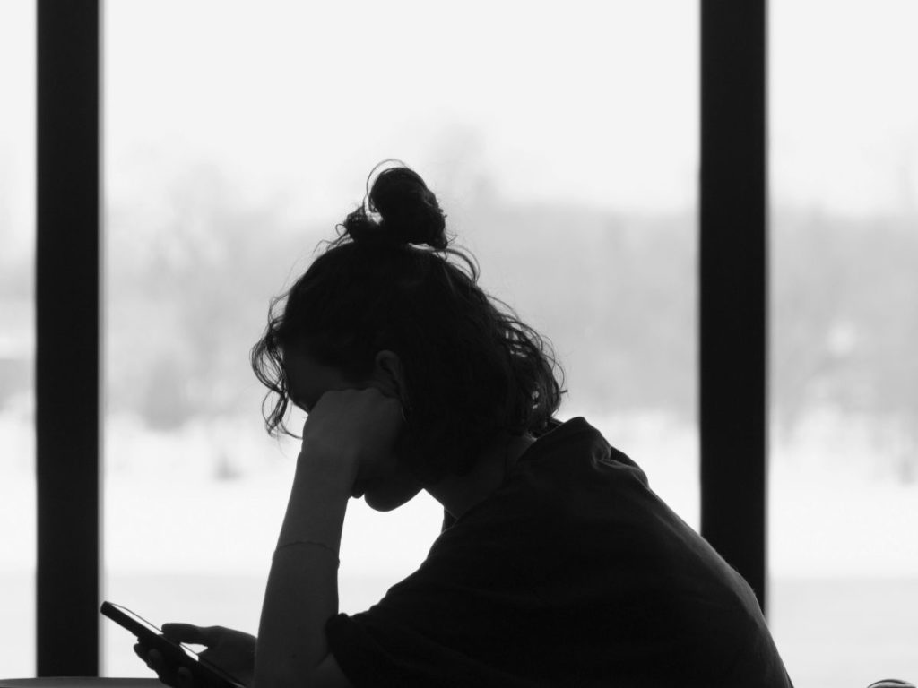 携帯を手に頭を抱える女性の写真